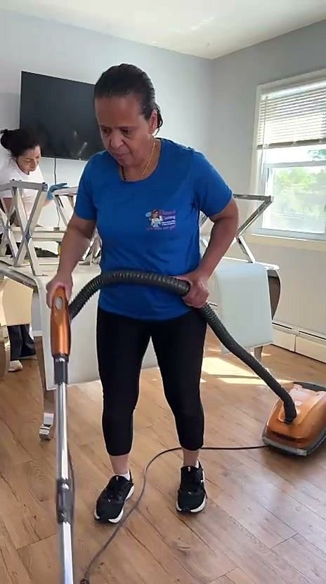 A uniformed team member vacuuming the floor with chairs lifted onto the table